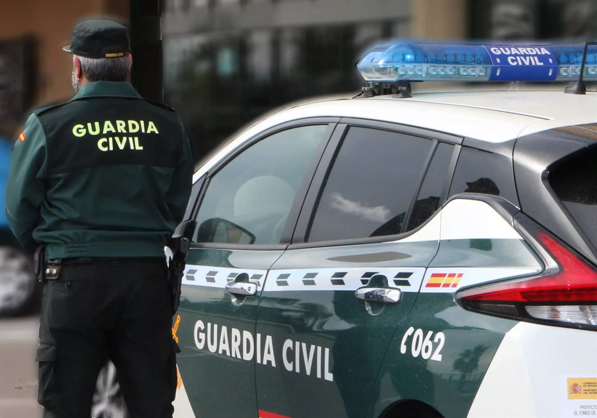 Un agente de la Guardia Civil, de espaldas, de pie junto a un vehículo oficial