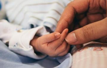 Un bebé de pocos días de edad coge el dedo de su madre.