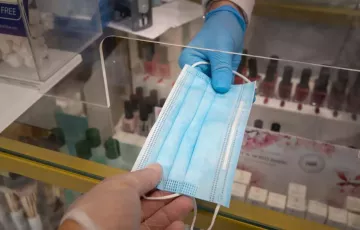 Entrega de una mascarilla quirúrgica en una farmacia. 