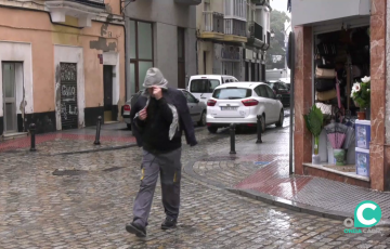 Un viandante se refugia de las inclemencias en la calle La Rosa