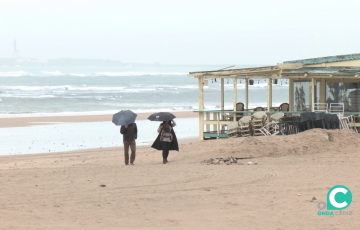 Dos paseantes se protegen de las inclemencias meteorológicas en la playa este lunes