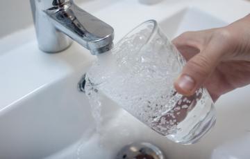 Una persona llena un vaso de agua de un grifo