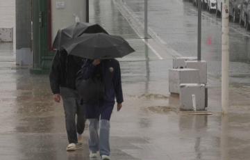 Dos viandantes circulan por el Paseo Marítimo bajo la lluvia