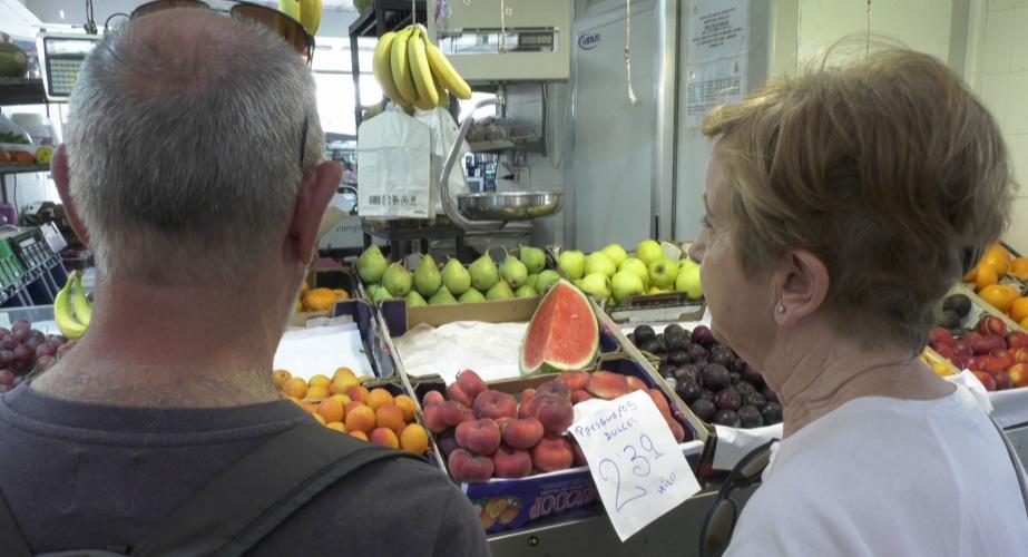 Clientes del Mercado Central junto a un puesto de frutas y verduras. 
