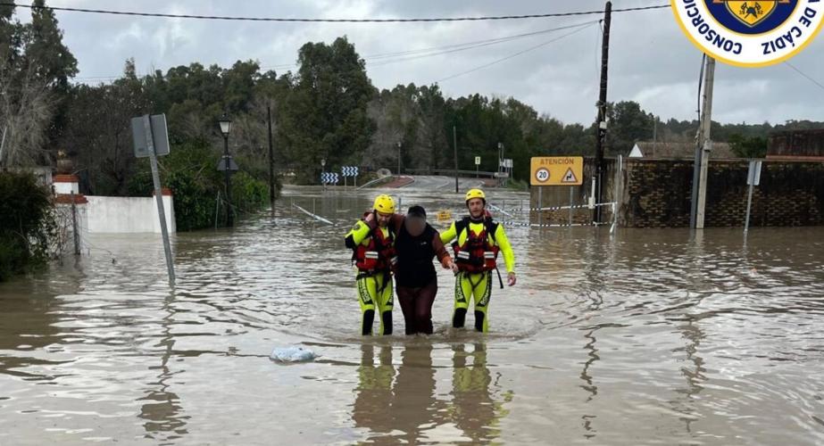 Dos bomberos ayudan a una persona en Arcos a salir de la zona inundada con motivo de la crecida del agua por la apertura de la presa