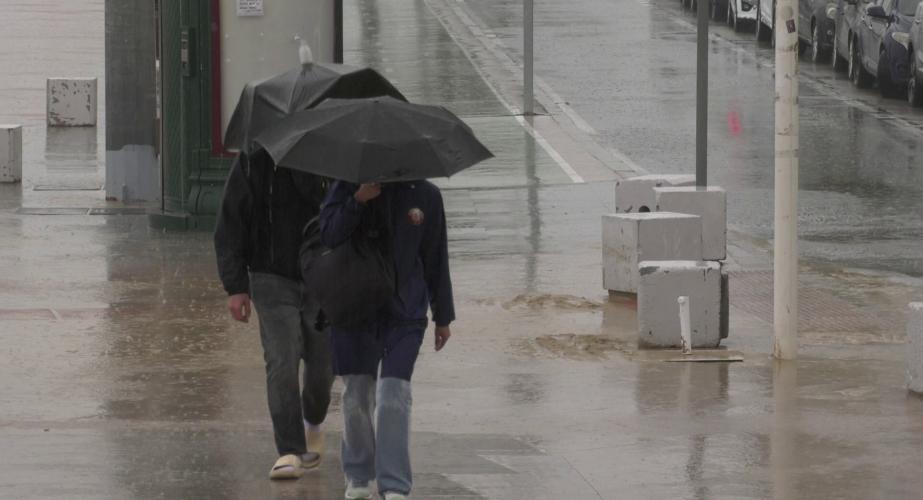 Dos viandantes circulan por el Paseo Marítimo bajo la lluvia