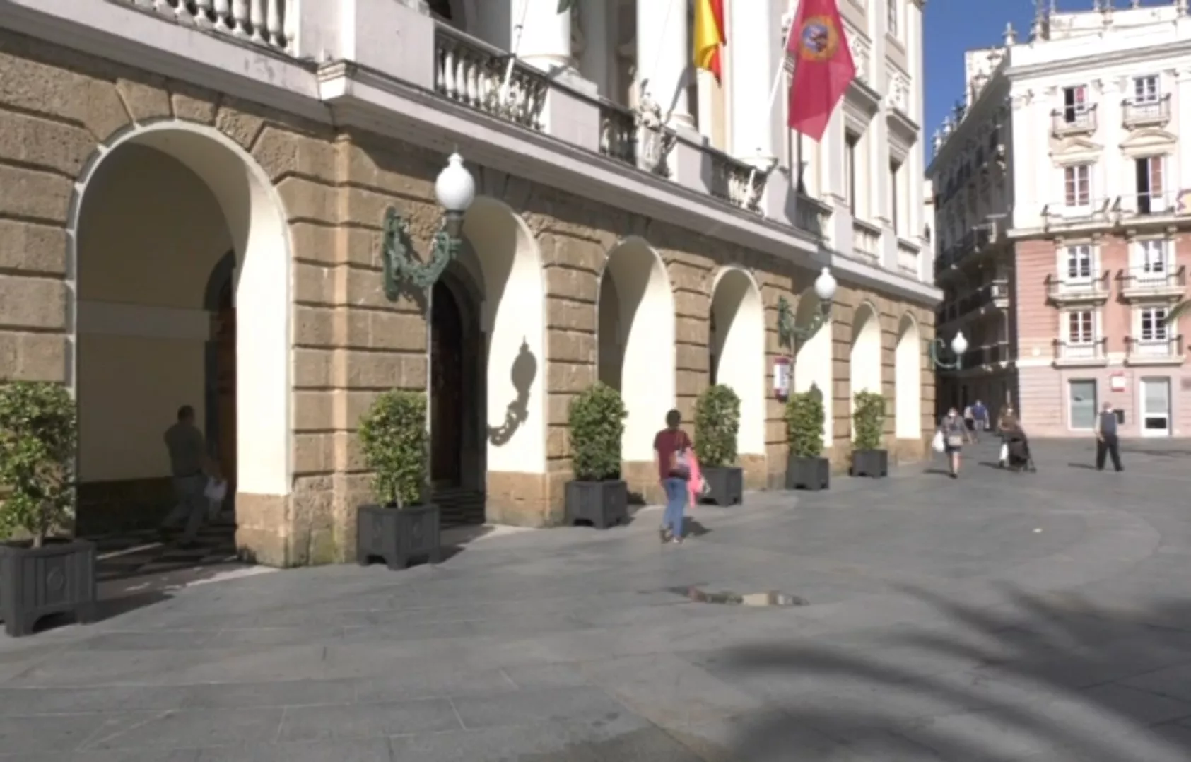 Varias personas pasan por delante del ayuntamiento en la plaza de San Juan de Dios