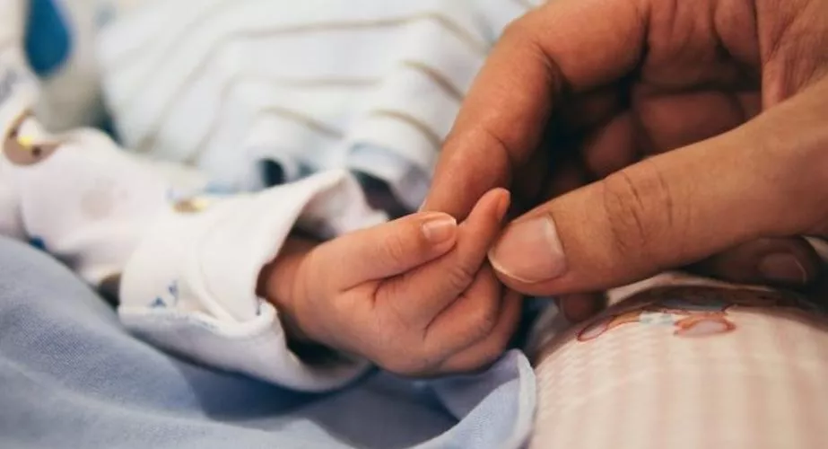 Un bebé de pocos días de edad coge el dedo de su madre.