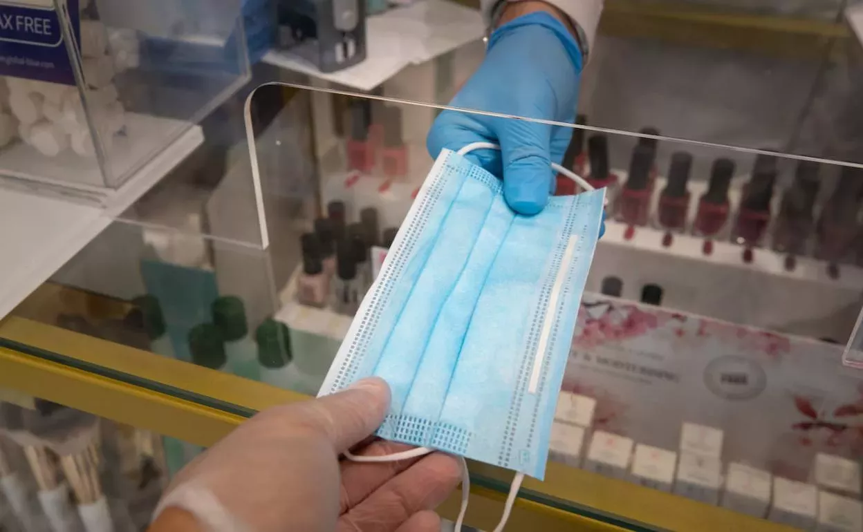 Entrega de una mascarilla quirúrgica en una farmacia. 