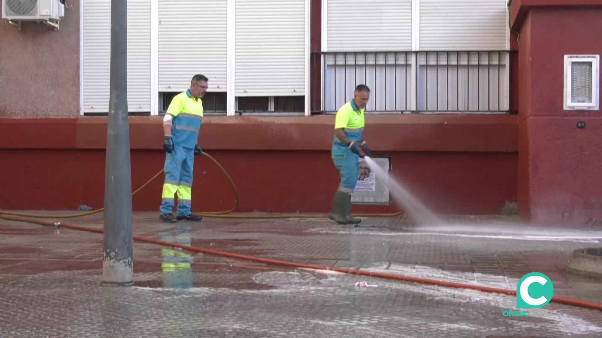 Dos operarios limpian el acerado bajo presión de agua