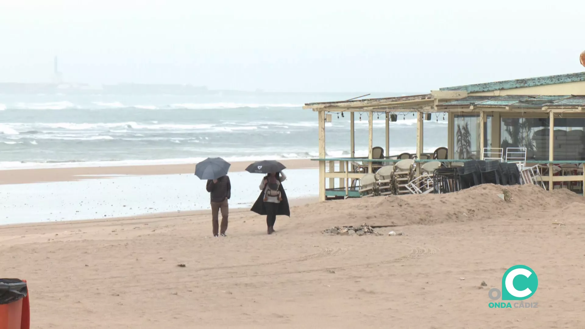 Dos paseantes se protegen de las inclemencias meteorológicas en la playa este lunes